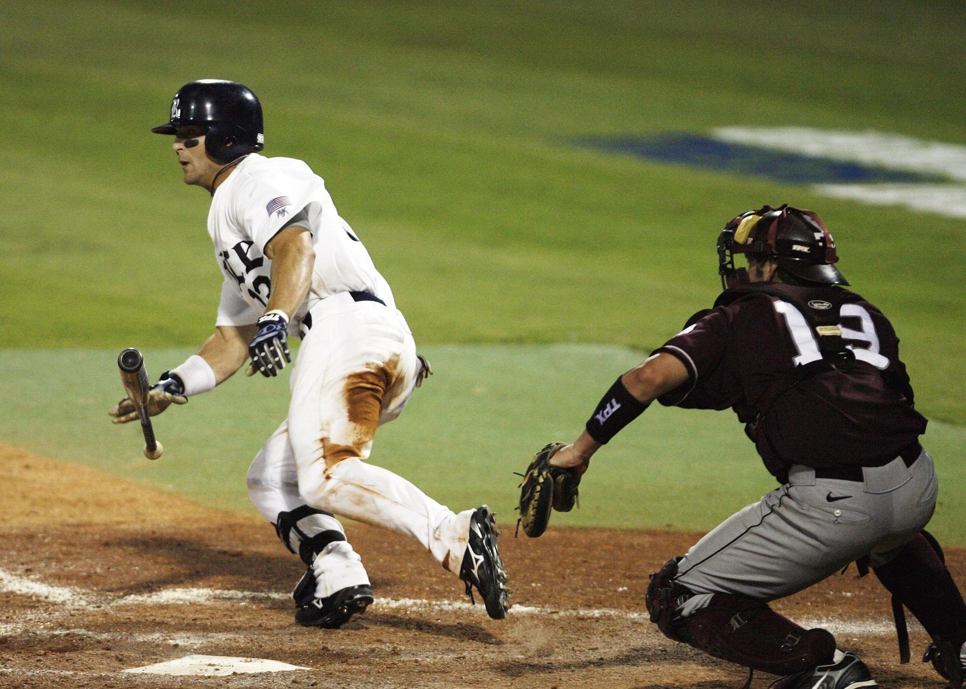 A baseball player begins running to first while dropping his bat.