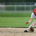 A baseball player leans down to scoop up the baseball.