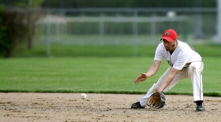 A baseball player leans down to scoop up the baseball.