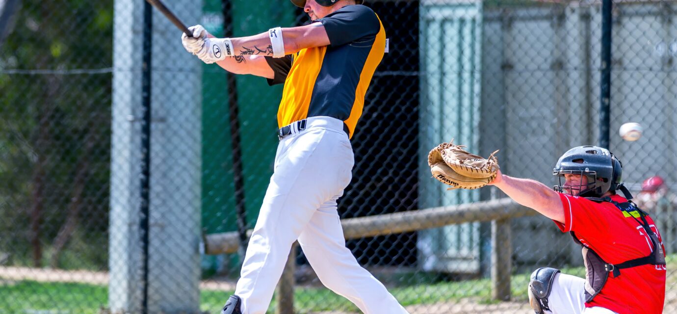 A batter swings with his bat, while the catcher raises his mitt.