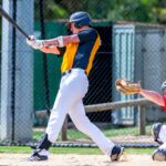 A batter swings with his bat, while the catcher raises his mitt.