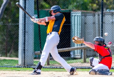 A batter swings with his bat, while the catcher raises his mitt.