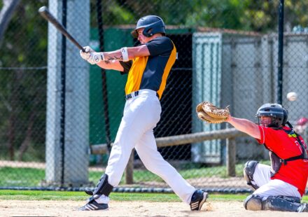 A batter swings with his bat, while the catcher raises his mitt.