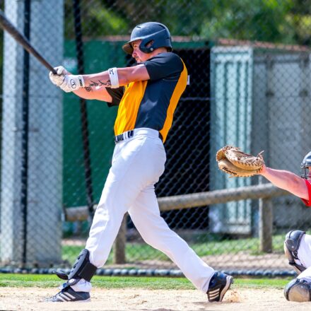 A batter swings with his bat, while the catcher raises his mitt.