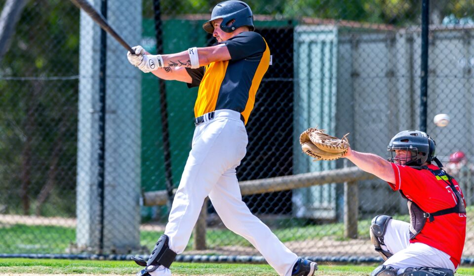A batter swings with his bat, while the catcher raises his mitt.