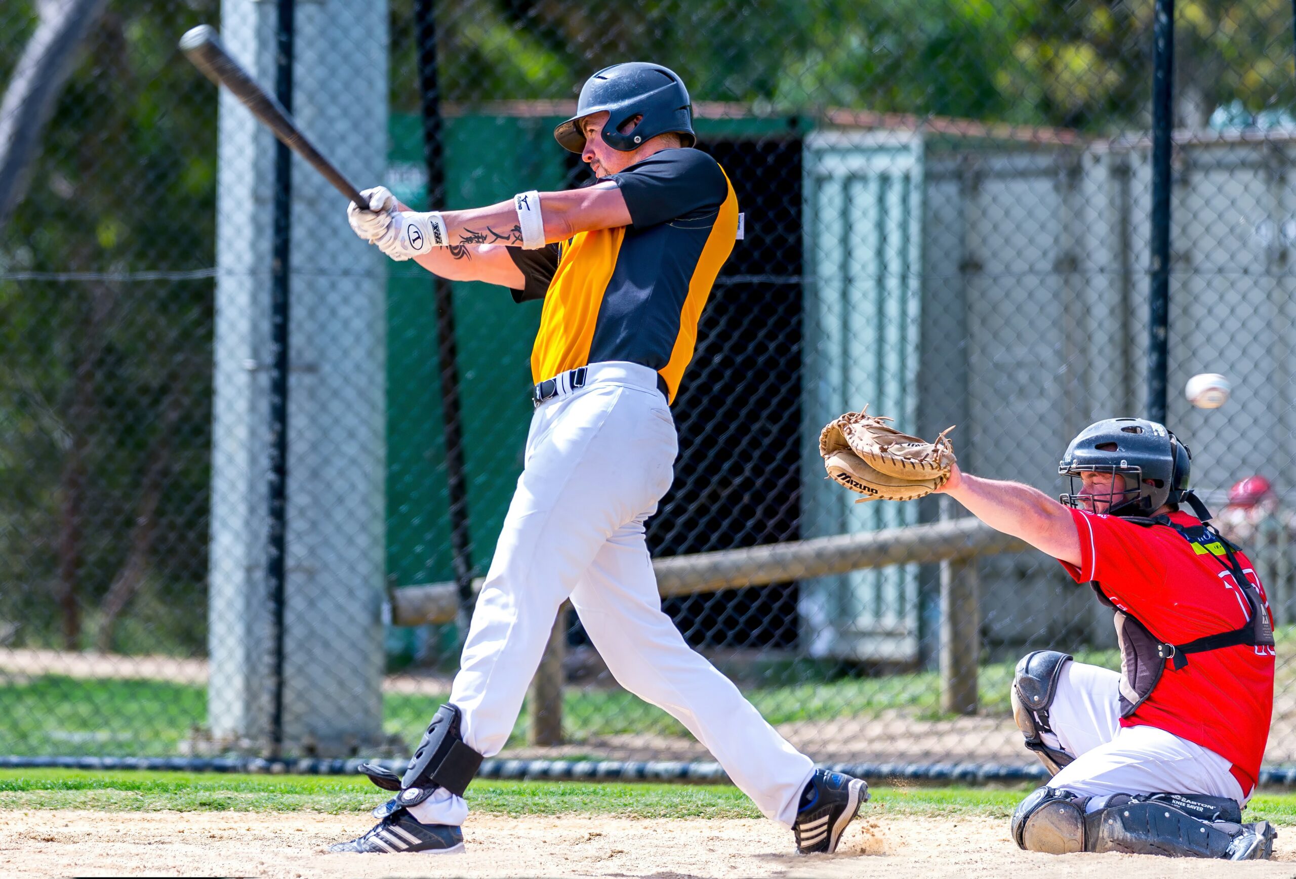 A batter swings with his bat, while the catcher raises his mitt.