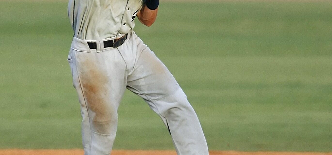 A baseball player leaps while throwing the ball.