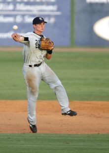 A baseball player leaps while throwing the ball.