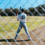A baseball player is seen beyond a fence holding his bat.