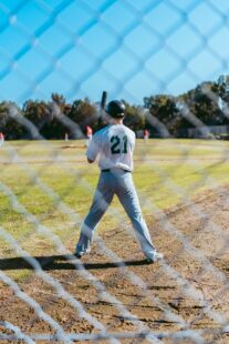 A baseball player is seen beyond a fence holding his bat.