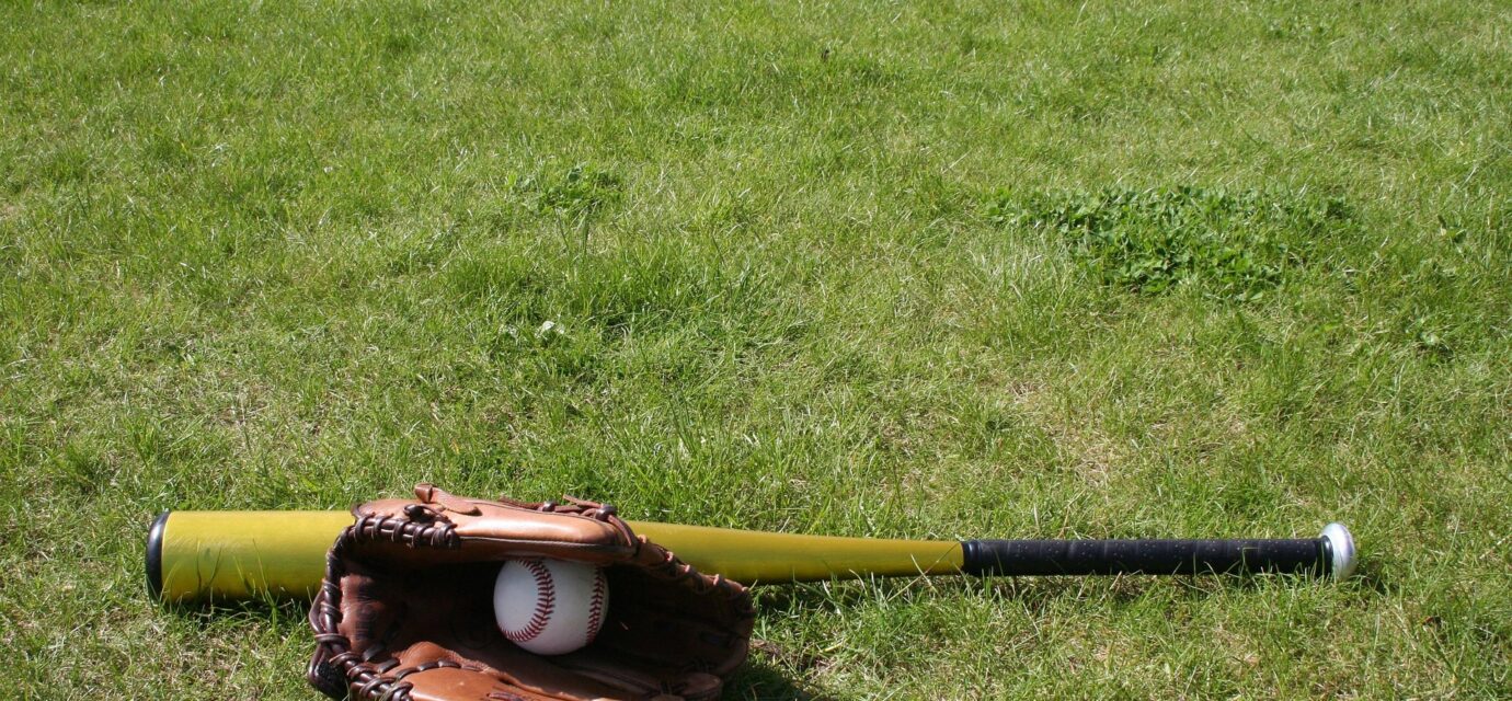 A baseball bat and mitt with a ball are on the grass.