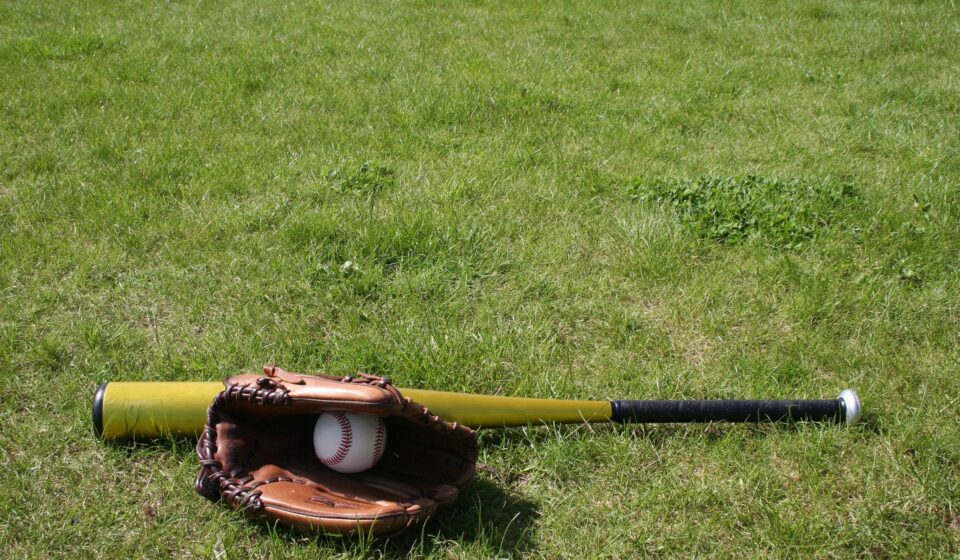 A baseball bat and mitt with a ball are on the grass.