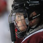 A baseball catcher looks out through his face mask.