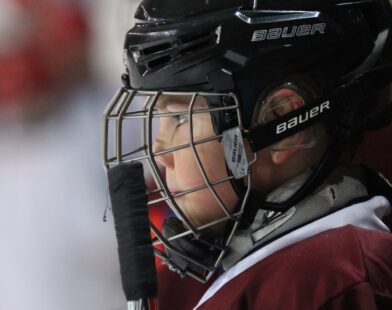 A baseball catcher looks out through his face mask.