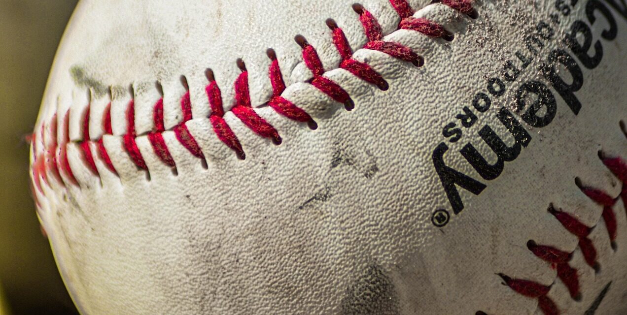 Several baseballs rest in the grass.