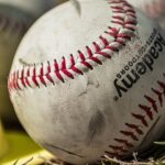 Several baseballs rest in the grass.