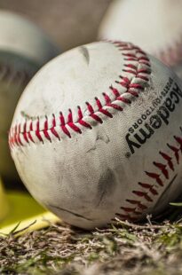 Several baseballs rest in the grass.