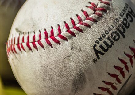 Several baseballs rest in the grass.