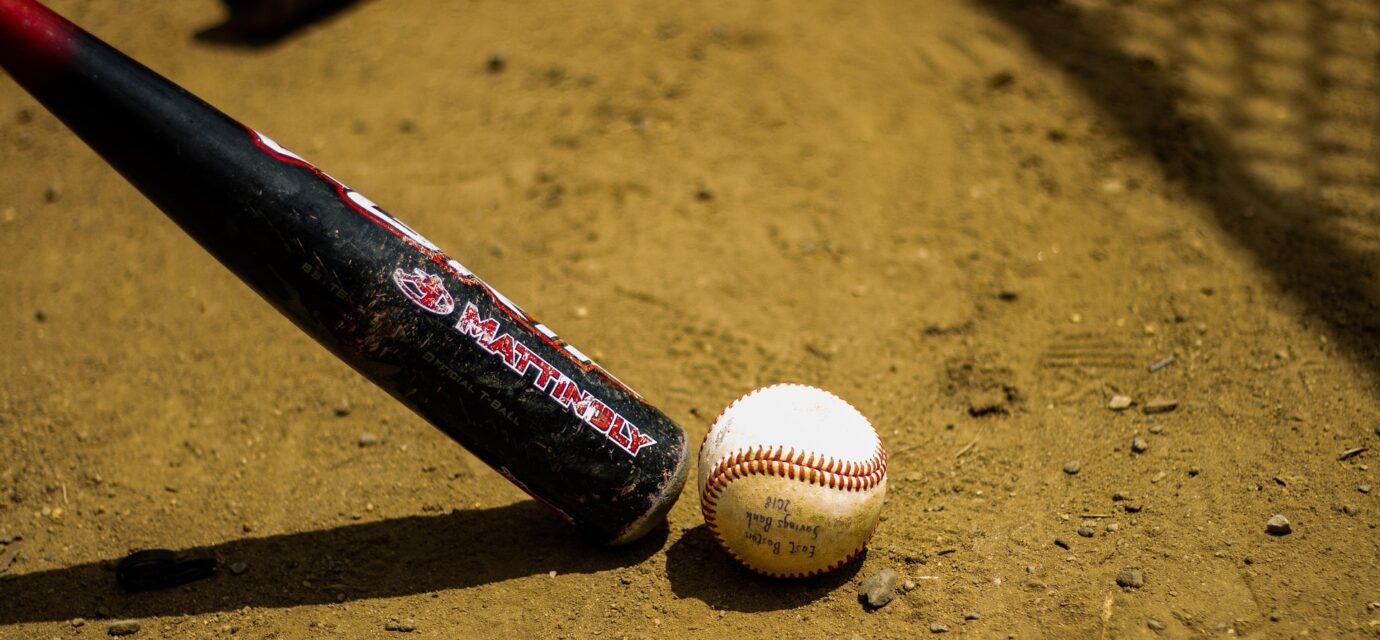 A baseball bat and ball are in the dirt in front of a chain-link fence.