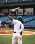 A baseball player swings a bat over his head.