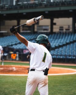 A baseball player swings a bat over his head.