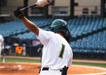 A baseball player swings a bat over his head.