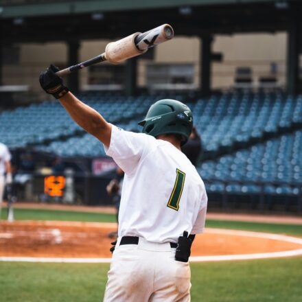 A baseball player swings a bat over his head.
