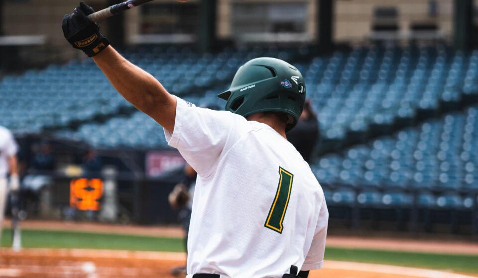 A baseball player swings a bat over his head.