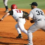A runner races to the base while the infielder waits for the ball.