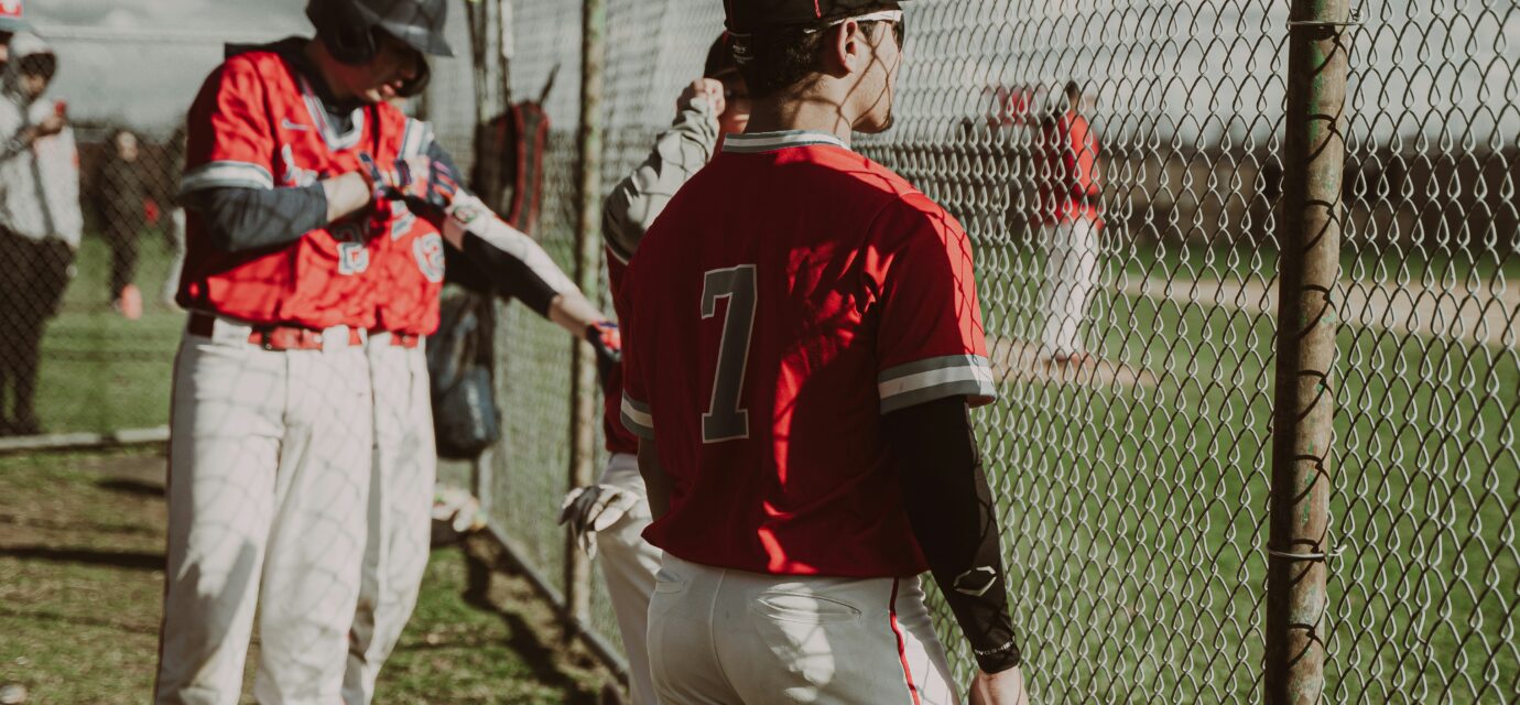 Baseball players watch the game through a chain-link fence.