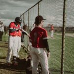 Baseball players watch the game through a chain-link fence.