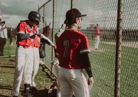 Baseball players watch the game through a chain-link fence.