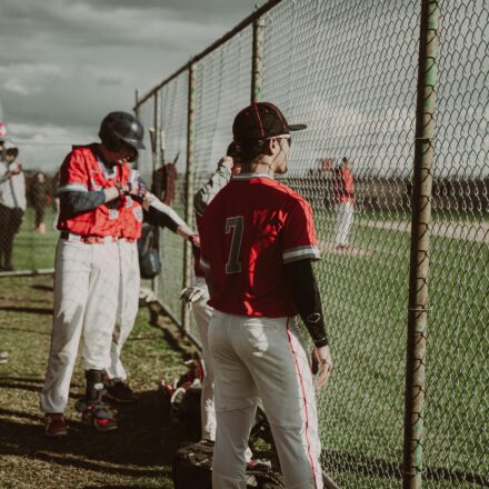 Baseball players watch the game through a chain-link fence.