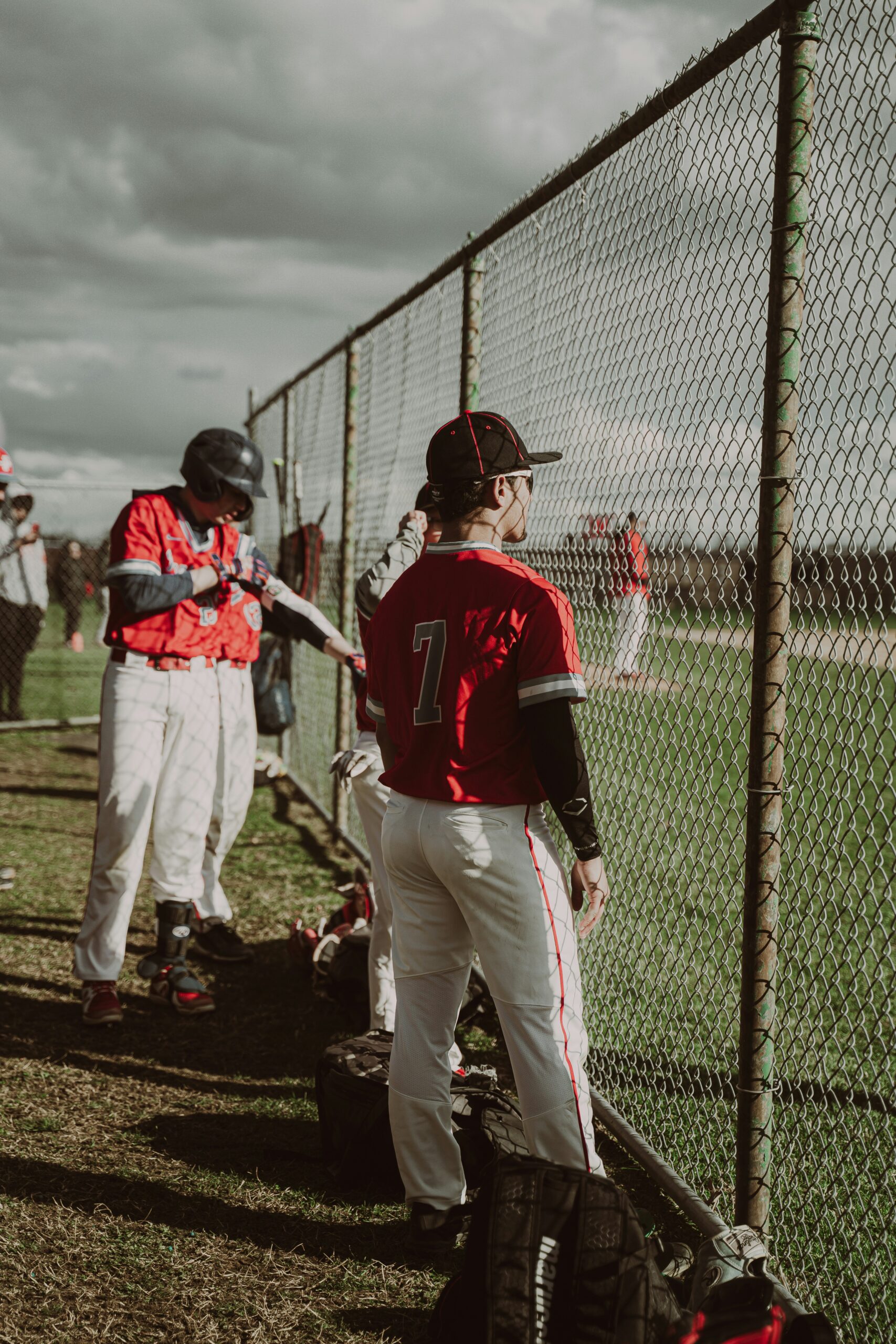 Baseball players watch the game through a chain-link fence.