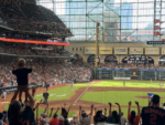 Fans cheer during an Astros game at Daikin Park as a child raises both arms in celebration.