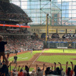 Fans cheer during an Astros game at Daikin Park as a child raises both arms in celebration.