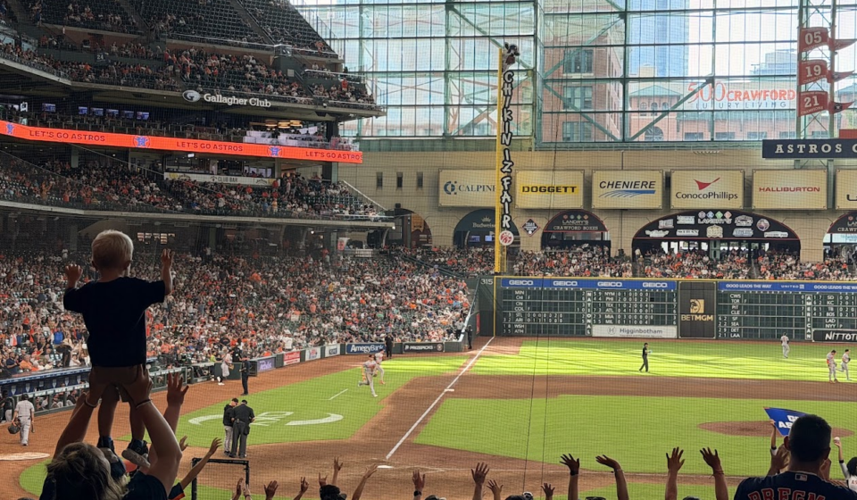 Fans cheer during an Astros game at Daikin Park as a child raises both arms in celebration.
