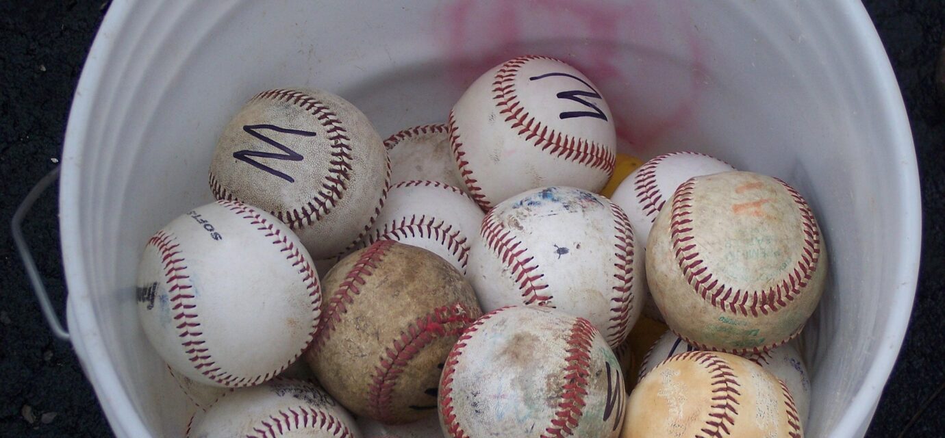 Looking down into a bucket of mixed baseballs.
