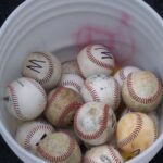 Looking down into a bucket of mixed baseballs.