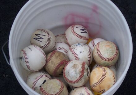 Looking down into a bucket of mixed baseballs.