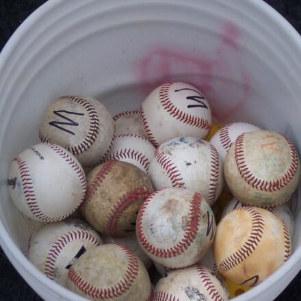 Looking down into a bucket of mixed baseballs.