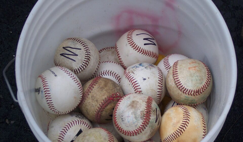 Looking down into a bucket of mixed baseballs.
