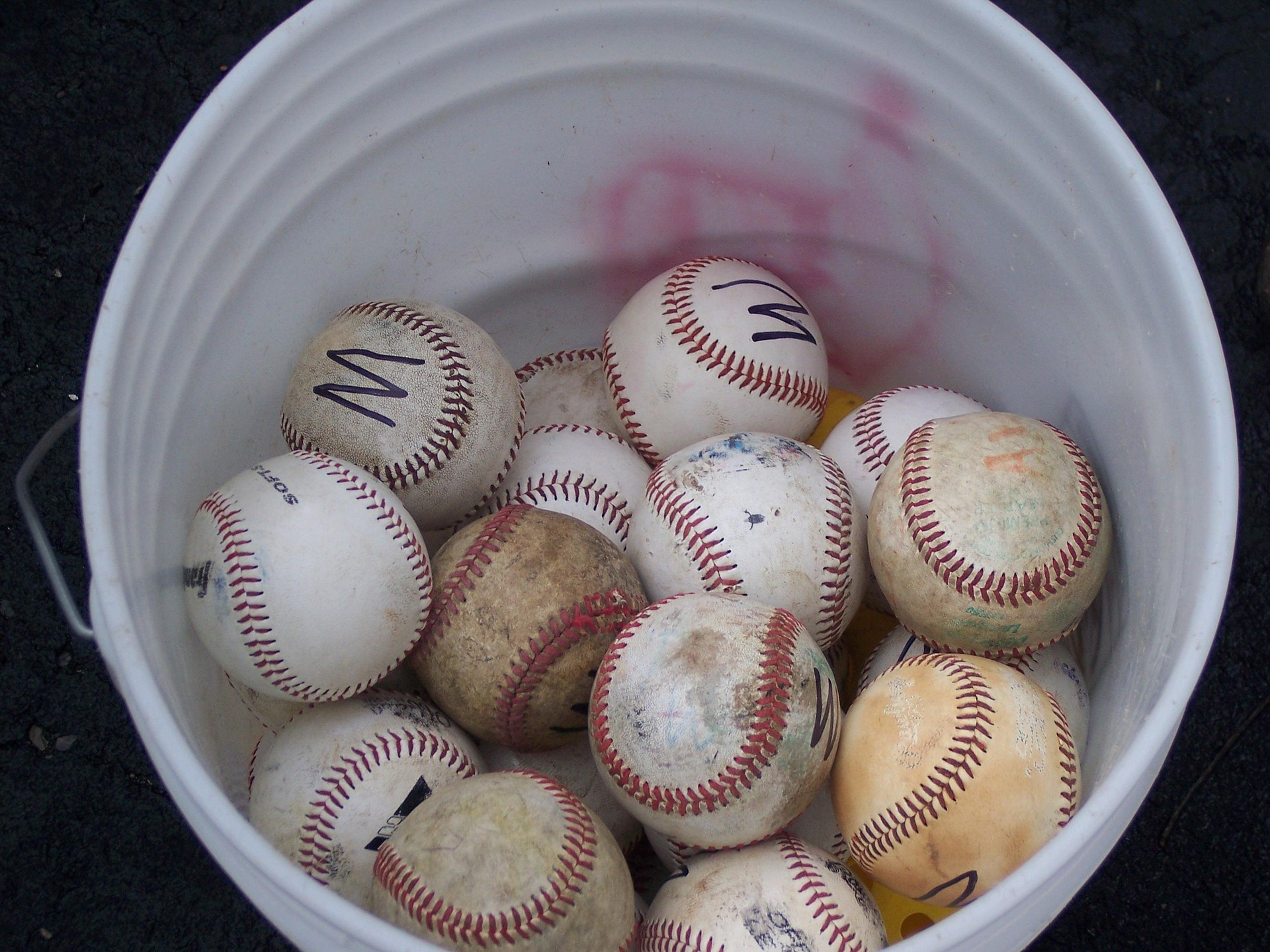 Looking down into a bucket of mixed baseballs.