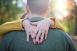 Woman showing an engagement ring while embracing her partner outdoors.