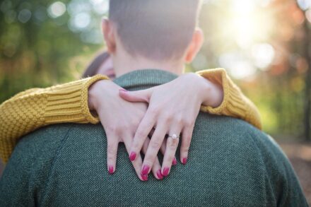 Woman showing an engagement ring while embracing her partner outdoors.