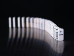 A single white domino stands in front of a long curved line of dominoes against a dark background.