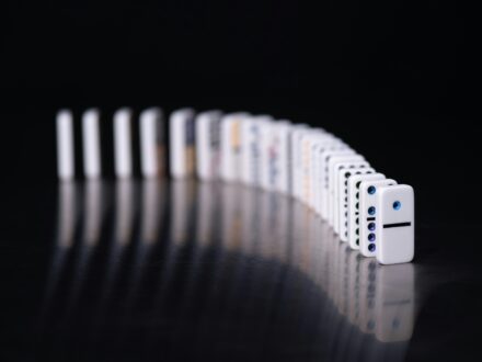 A single white domino stands in front of a long curved line of dominoes against a dark background.
