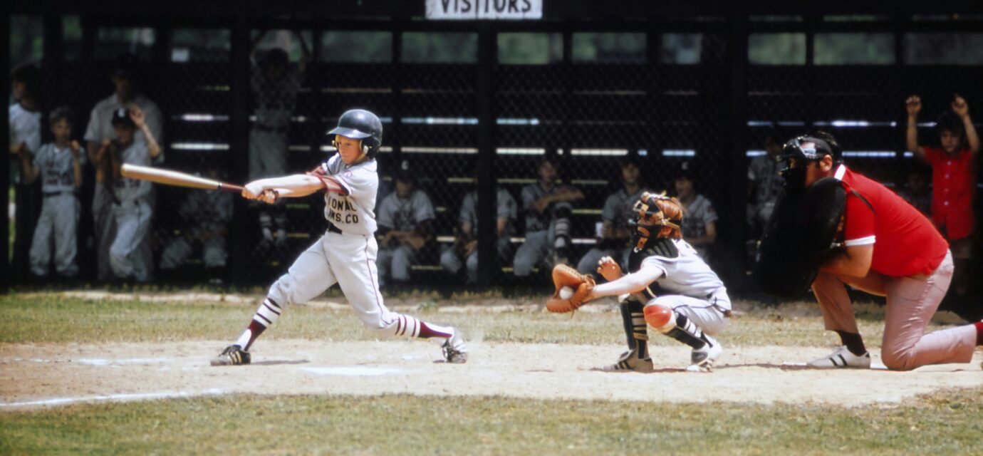 A baseball player swings at a pitch while the catcher receives the ball and the umpire watches from behind home plate.