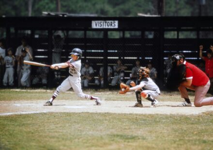 A baseball player swings at a pitch while the catcher receives the ball and the umpire watches from behind home plate.