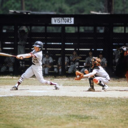 A baseball player swings at a pitch while the catcher receives the ball and the umpire watches from behind home plate.